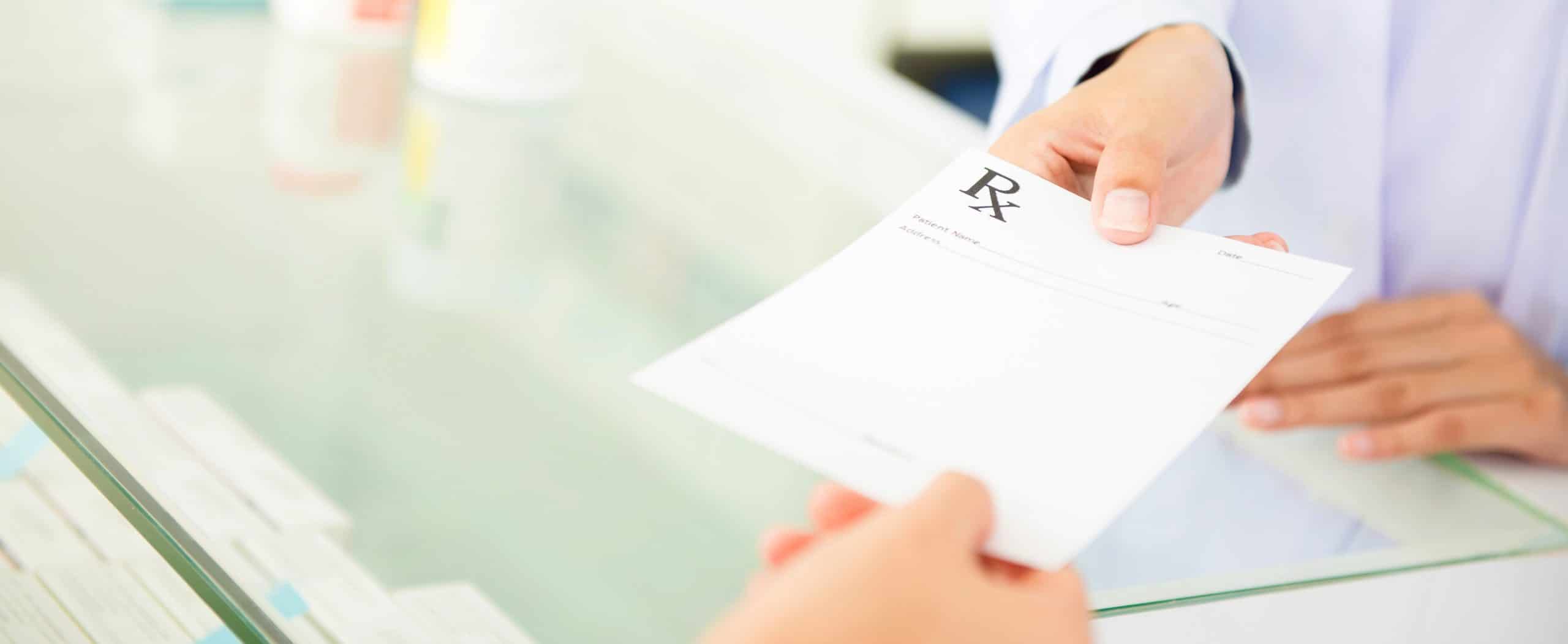 A patients hands a prescription to a pharmacy professional.