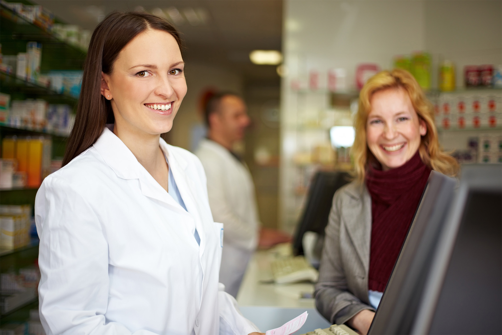 A female pharmacist and a female patient smile while standing at the pharmacy counter