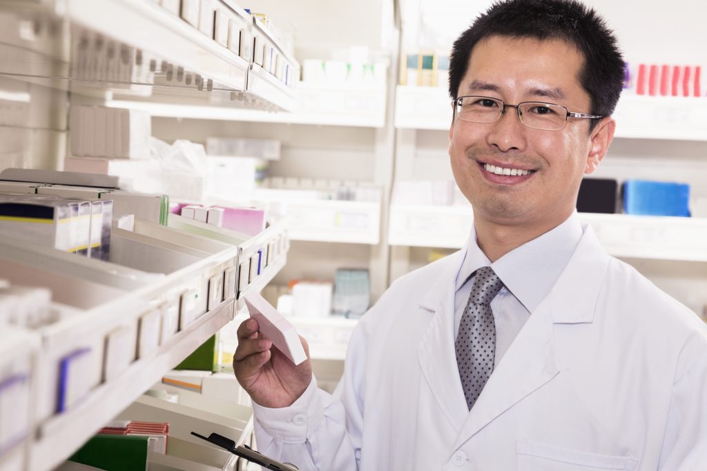 Male pharmacist selects a drug from a dispensary shelf