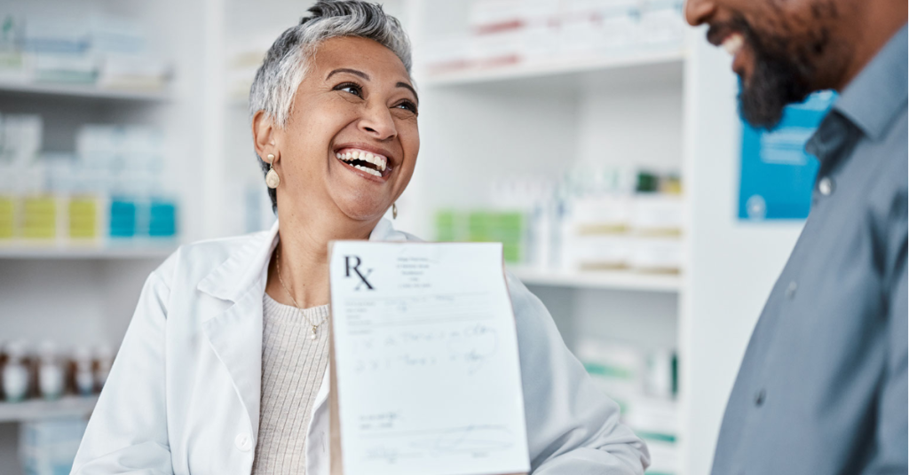 A pharmacists smiles at a patient during prescription pick-up at a community pharmacy.
