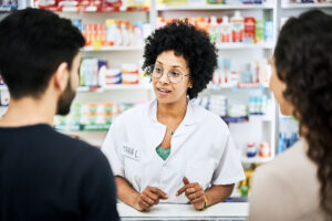 A pharmacy professional talks with a patient and support person across the pharmacy counter.