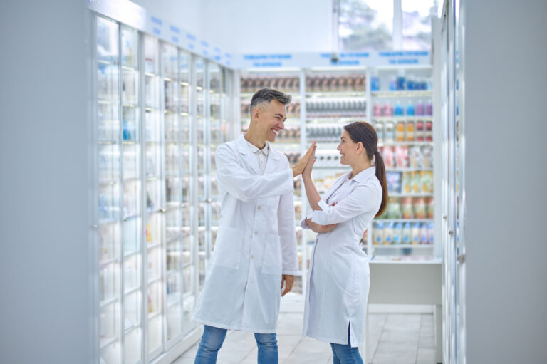 Two people in lab coats feeling good and smiling, giving one other a high-five.