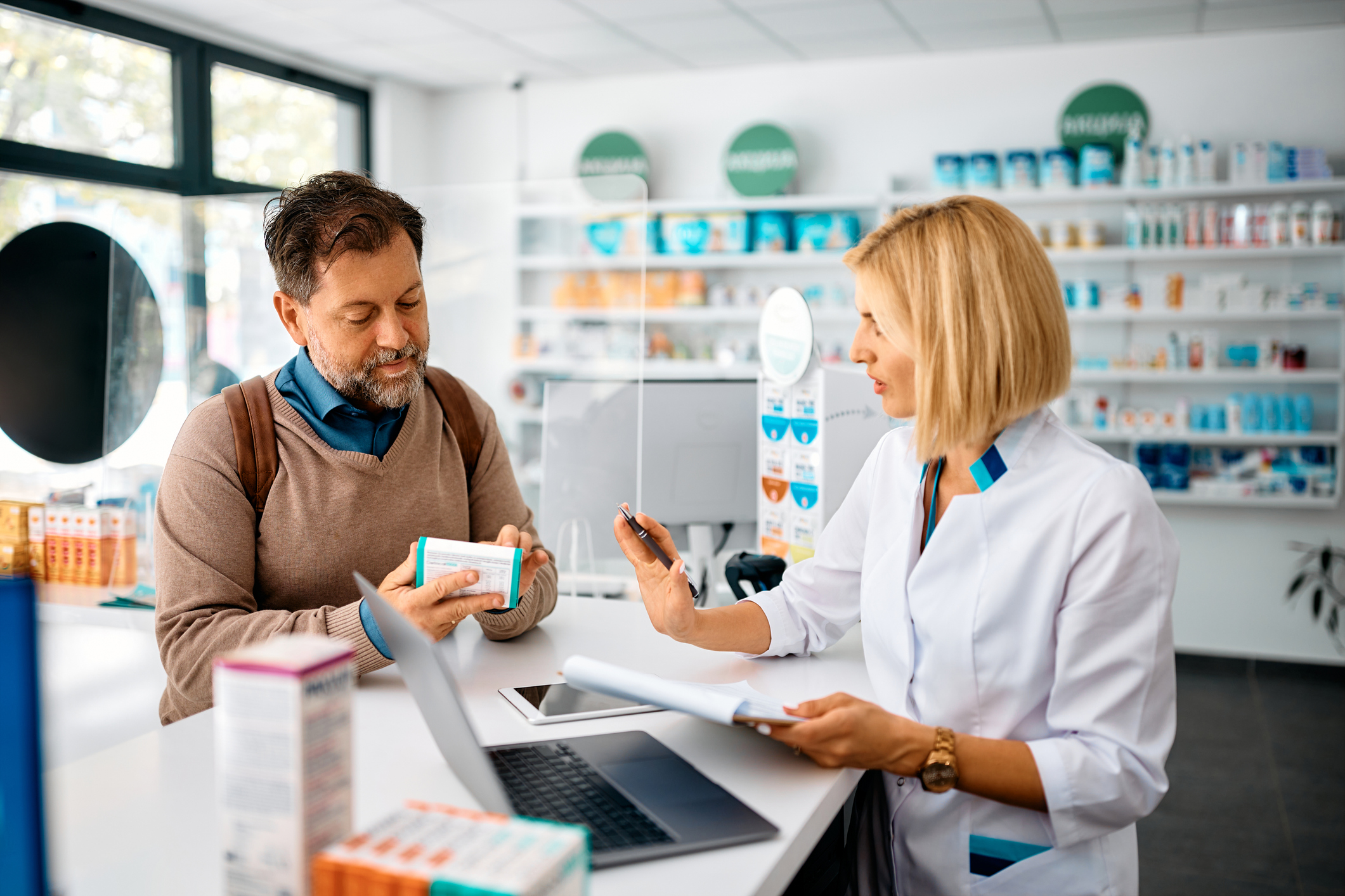 A female pharmacist apologizing to a male patient inside a pharmacy.